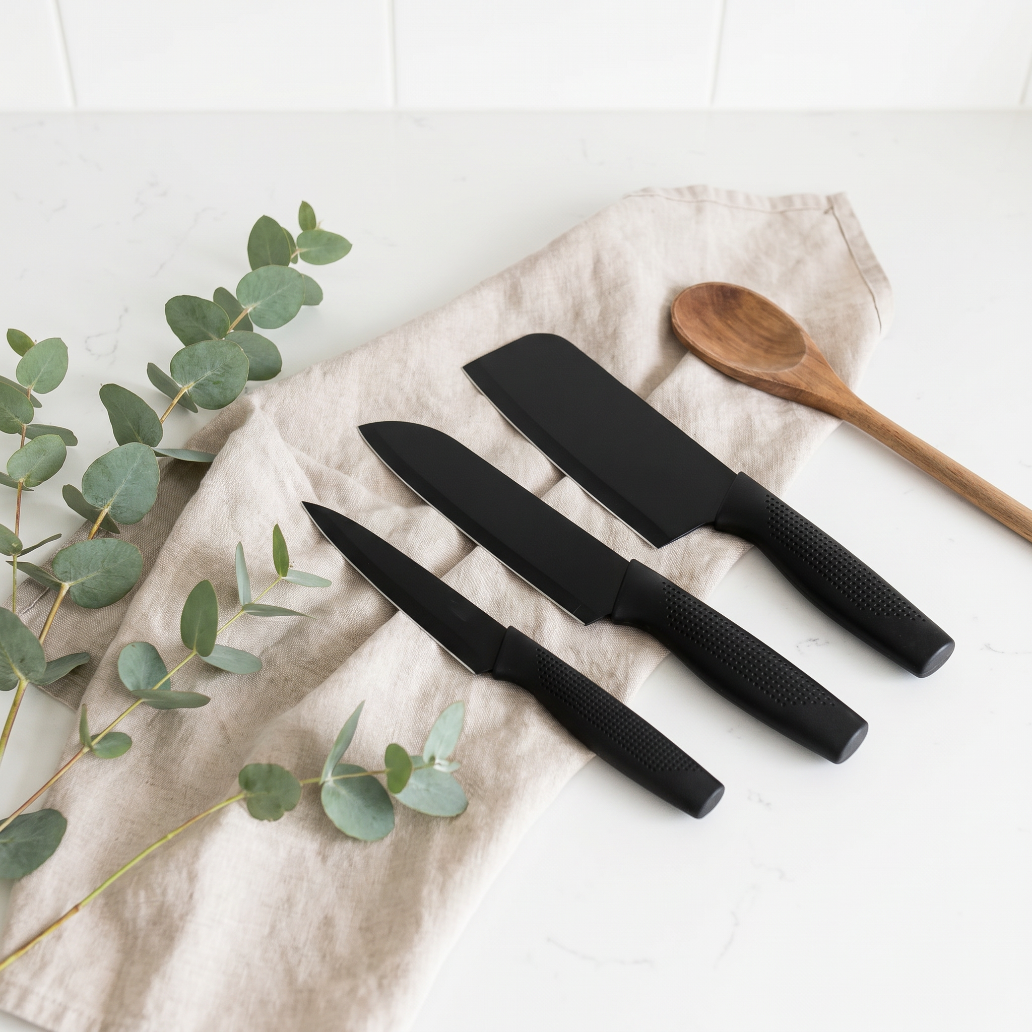 AI Design for Place the knives on a white countertop with a beige linen cloth, wooden spoon, and eucalyptus leaves. Keep the composition airy and uncluttered so all three knives stand out naturally while creating a clean Scandinavian-inspired kitchen atmosphere.