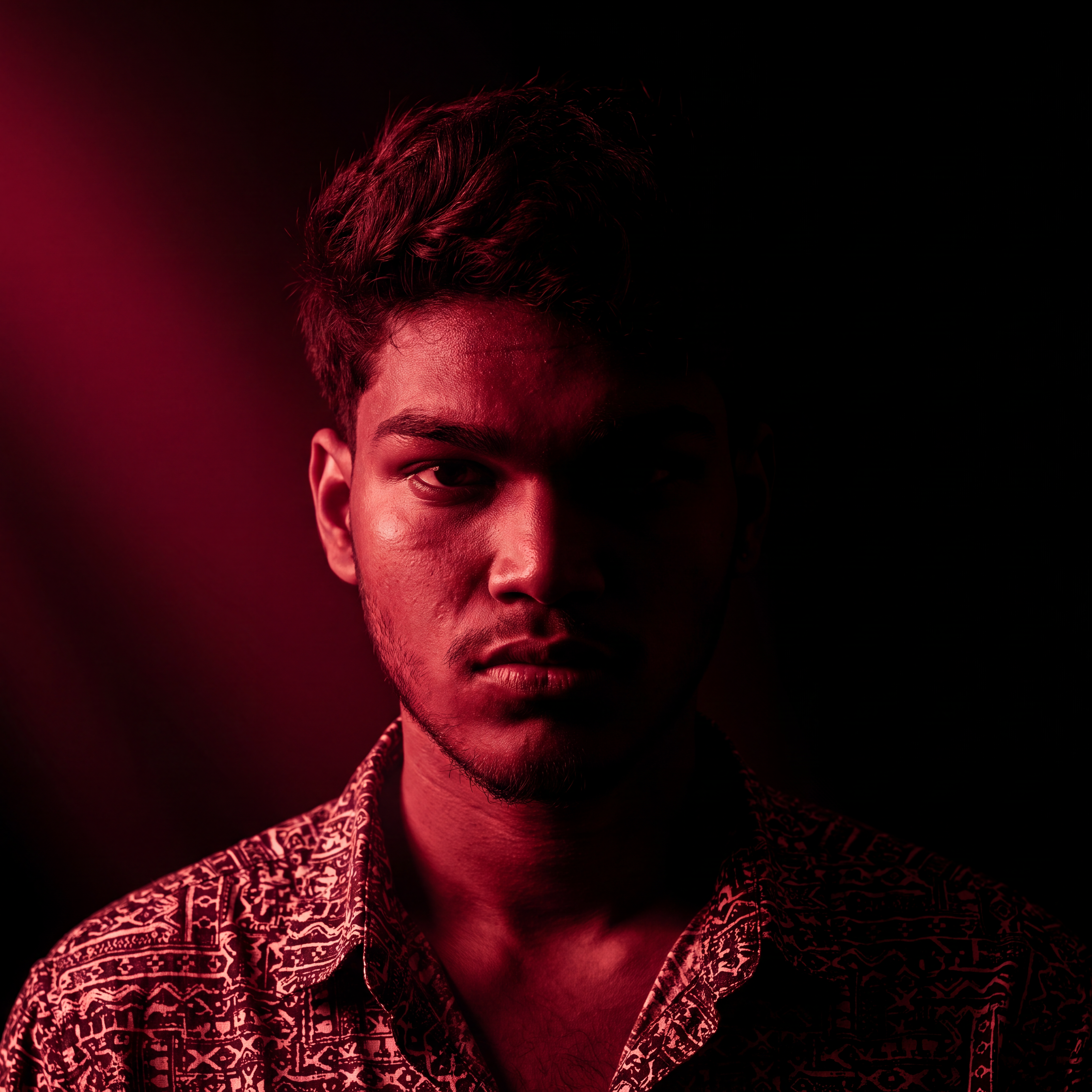 AI Design for Cinematic portrait, straight-on facial expression, hyper-realistic skin texture. Dramatic duotone lighting using only deep matte black (#000000) and rich crimson red (#B00020). Intense crimson directional side lighting sculpting the cheekbones, jawline, and hair texture, transitioning into deep black shadows on the opposite side. Minimalist, solid black background. Premium luxury fashion editorial aesthetic, high-contrast film noir style, sharp facial details, volumetric lighting, 8k resolution, photorealistic, no text, no logos. Use the attached image as the primary composition and structural reference.