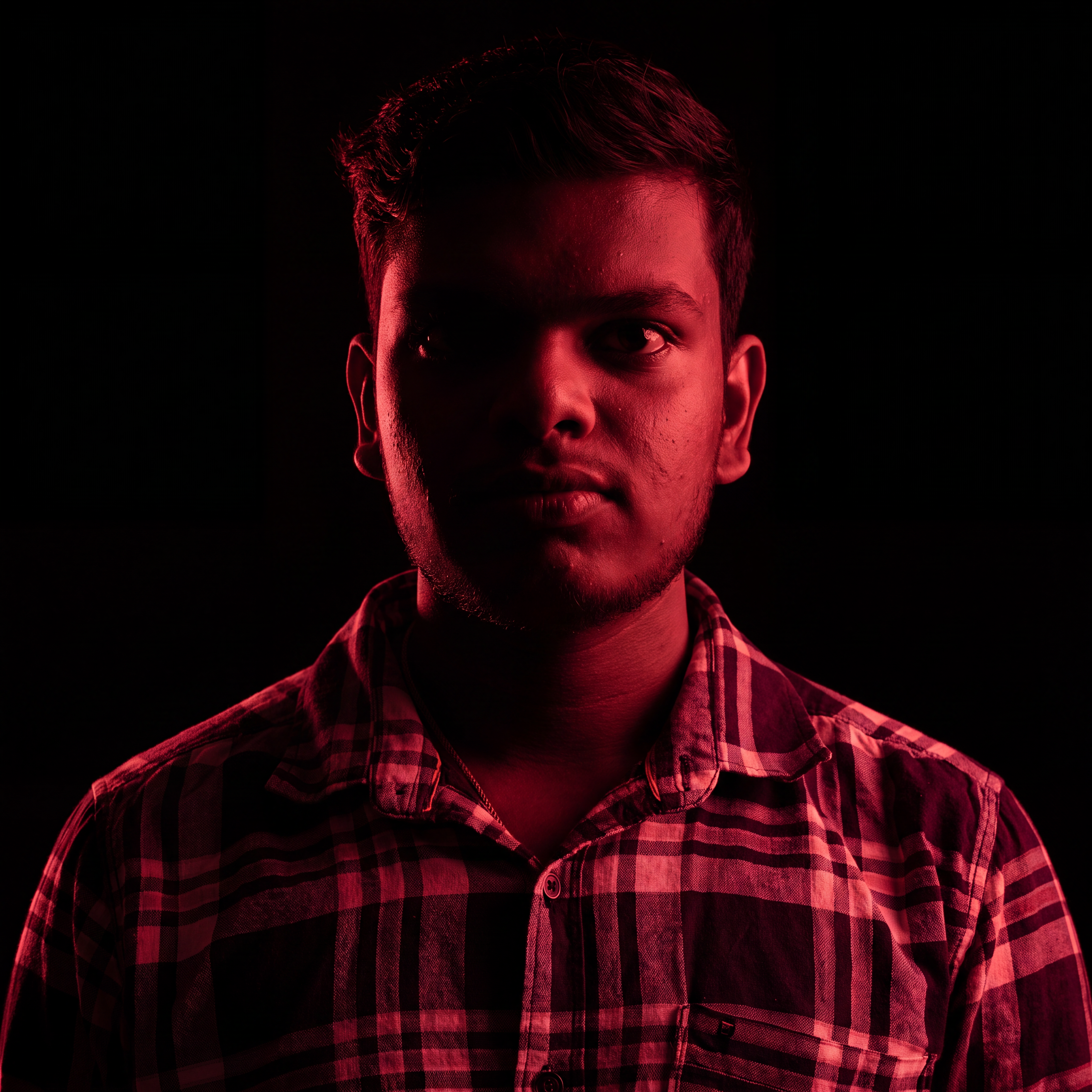 AI Design for Cinematic portrait, straight-on facial expression, hyper-realistic skin texture. Dramatic duotone lighting using only deep matte black (#000000) and rich crimson red (#B00020). Intense crimson directional side lighting sculpting the cheekbones, jawline, and hair texture, transitioning into deep black shadows on the opposite side. Minimalist, solid black background. Premium luxury fashion editorial aesthetic, high-contrast film noir style, sharp facial details, volumetric lighting, 8k resolution, photorealistic, no text, no logos. Use the attached image as the primary composition and structural reference.