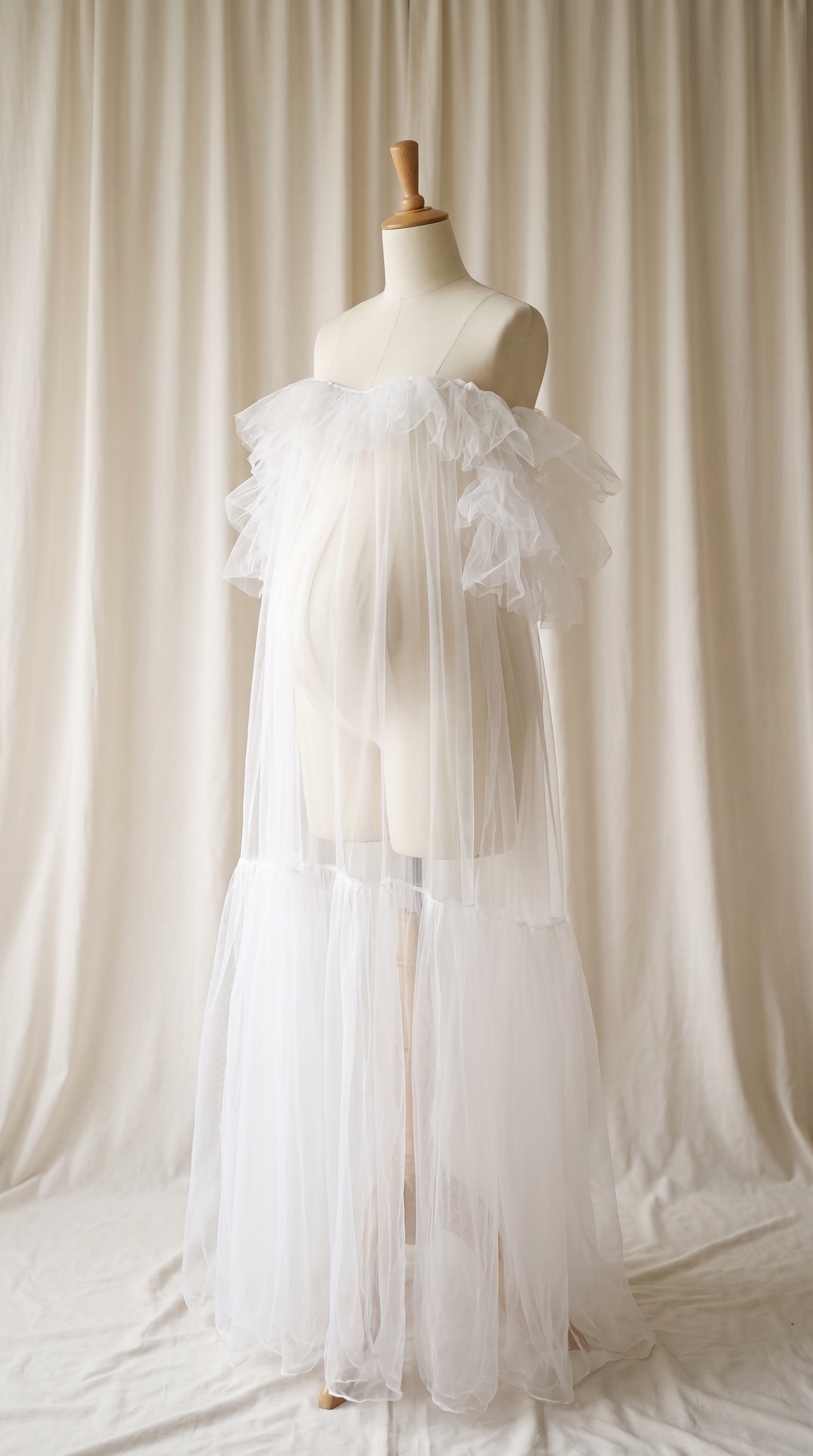 AI Design for 

{
  "task": "Reference-guided maternity garment transfer and studio background replacement",
  "reference_image": "[Attach the original maternity dress photograph]",
  "prompt": "Create a photorealistic maternity fashion product photograph using the attached image as the authoritative garment reference. Transfer the existing dress onto the specified pregnant tailor's dress form; do not create a similar dress, reinterpret the design, beautify it, or redesign it. Change only the original wearer or display form and the surrounding environment. Garment fidelity takes priority over styling and aesthetics. Follow the preservation, mannequin, background, lighting, and framing requirements below.",
  "garment_preservation": {
    "preserve": "Match the visible reference faithfully: hue, saturation, tonal relationships, fabric texture and weight, weave, sheen, transparency, print scale and placement, lace motifs, embroidery, embellishments, seams, neckline, bodice construction, waistline, sleeve cut and length, cuffs, hem, skirt volume, dress length, and any existing train.",
    "fit_and_drape": "Allow only the physically necessary changes in folds and tension caused by fitting the garment to the pregnant form. Preserve the garment's construction and overall silhouette. Fabric must respond naturally to gravity and belly volume, without stretching prints, melting lace, or distorting seams. Support the sleeves naturally without visible arms, hands, rods, or stuffing.",
    "uncertainty": "Do not invent decorative details or unseen garment construction. Keep the reference viewing angle where possible. If the hem or train is cropped out, preserve a comparable crop rather than inventing its appearance. Do not add a train if none is shown."
  },
  "mannequin": {
    "type": "Classic vintage tailor's dress form with a realistic pregnant torso and softly rounded belly, standing upright and centered.",
    "finish": "Matte cream-ivory linen-covered body, gently rounded shoulder ends, and a small round natural-wood neck cap. No head, facial features, arms, hands, human skin, glossy plastic, or exaggerated anatomy.",
    "visibility": "The dress remains the visual focus. Show the form only where the garment naturally exposes it; do not alter the neckline or opacity to hide it. Keep any support discreet and mostly concealed by the garment."
  },
  "background": "A plain warm off-white ivory fabric curtain with soft vertical folds and subtle vintage texture, clean and unpatterned. Matching ivory fabric continues onto the floor in gentle natural folds, creating visual continuity without a hard horizon line. No furniture, props, decorative architecture, or additional objects.",
  "lighting": "Large, soft, diffused daylight from slightly above and to one side; gentle fill, delicate contact shadows, and natural depth. Neutral white balance preserves garment color. Maintain separation between the dress and ivory backdrop without changing either color. No harsh shadows, clipped highlights, strong color casts, or artificial glow.",
  "composition": "Portrait framing, centered subject, straight verticals, realistic proportions, and minimal perspective distortion. Show the complete dress and existing train when supported by the reference, with modest breathing room. Preserve a cropped composition when required to avoid inventing missing garment details.",
  "output": {
    "aspect_ratio": "16:21",
    "orientation": "portrait",
    "style": "High-detail photorealistic product photography; crisp textile detail, natural tonal transitions, no CGI appearance."
  },
  "negative_prompt": "human model, head, face, hair, arms, hands, exposed human skin, non-pregnant torso, oversized belly, glossy plastic mannequin, redesigned dress, altered neckline, missing sleeves, added sleeves, changed hem, invented train, changed color, incorrect print scale, misplaced pattern, missing embellishments, added decorations, warped seams, melted lace, floating fabric, artificial transparency, clutter, furniture, luxury interior, text, logo, watermark, harsh flash, yellow color cast, oversaturation, blur, excessive smoothing, CGI, illustration"
}
