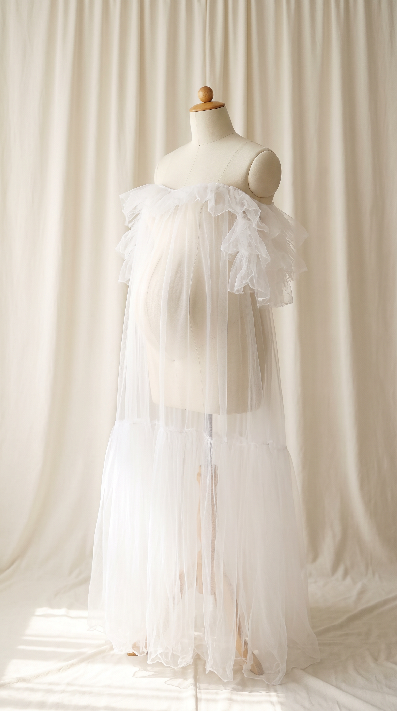AI Design for 

{
  "task": "Reference-guided maternity garment transfer and studio background replacement",
  "reference_image": "[Attach the original maternity dress photograph]",
  "prompt": "Create a photorealistic maternity fashion product photograph using the attached image as the authoritative garment reference. Transfer the existing dress onto the specified pregnant tailor's dress form; do not create a similar dress, reinterpret the design, beautify it, or redesign it. Change only the original wearer or display form and the surrounding environment. Garment fidelity takes priority over styling and aesthetics. Follow the preservation, mannequin, background, lighting, and framing requirements below.",
  "garment_preservation": {
    "preserve": "Match the visible reference faithfully: hue, saturation, tonal relationships, fabric texture and weight, weave, sheen, transparency, print scale and placement, lace motifs, embroidery, embellishments, seams, neckline, bodice construction, waistline, sleeve cut and length, cuffs, hem, skirt volume, dress length, and any existing train.",
    "fit_and_drape": "Allow only the physically necessary changes in folds and tension caused by fitting the garment to the pregnant form. Preserve the garment's construction and overall silhouette. Fabric must respond naturally to gravity and belly volume, without stretching prints, melting lace, or distorting seams. Support the sleeves naturally without visible arms, hands, rods, or stuffing.",
    "uncertainty": "Do not invent decorative details or unseen garment construction. Keep the reference viewing angle where possible. If the hem or train is cropped out, preserve a comparable crop rather than inventing its appearance. Do not add a train if none is shown."
  },
  "mannequin": {
    "type": "Classic vintage tailor's dress form with a realistic pregnant torso and softly rounded belly, standing upright and centered.",
    "finish": "Matte cream-ivory linen-covered body, gently rounded shoulder ends, and a small round natural-wood neck cap. No head, facial features, arms, hands, human skin, glossy plastic, or exaggerated anatomy.",
    "visibility": "The dress remains the visual focus. Show the form only where the garment naturally exposes it; do not alter the neckline or opacity to hide it. Keep any support discreet and mostly concealed by the garment."
  },
  "background": "A plain warm off-white ivory fabric curtain with soft vertical folds and subtle vintage texture, clean and unpatterned. Matching ivory fabric continues onto the floor in gentle natural folds, creating visual continuity without a hard horizon line. No furniture, props, decorative architecture, or additional objects.",
  "lighting": "Large, soft, diffused daylight from slightly above and to one side; gentle fill, delicate contact shadows, and natural depth. Neutral white balance preserves garment color. Maintain separation between the dress and ivory backdrop without changing either color. No harsh shadows, clipped highlights, strong color casts, or artificial glow.",
  "composition": "Portrait framing, centered subject, straight verticals, realistic proportions, and minimal perspective distortion. Show the complete dress and existing train when supported by the reference, with modest breathing room. Preserve a cropped composition when required to avoid inventing missing garment details.",
  "output": {
    "aspect_ratio": "16:21",
    "orientation": "portrait",
    "style": "High-detail photorealistic product photography; crisp textile detail, natural tonal transitions, no CGI appearance."
  },
  "negative_prompt": "human model, head, face, hair, arms, hands, exposed human skin, non-pregnant torso, oversized belly, glossy plastic mannequin, redesigned dress, altered neckline, missing sleeves, added sleeves, changed hem, invented train, changed color, incorrect print scale, misplaced pattern, missing embellishments, added decorations, warped seams, melted lace, floating fabric, artificial transparency, clutter, furniture, luxury interior, text, logo, watermark, harsh flash, yellow color cast, oversaturation, blur, excessive smoothing, CGI, illustration"
}
