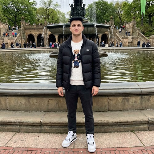 AI Design for Szerkeszd meg ezt a képet úgy hogy állok 1 helyen Newyorkba valami szép szökőkutnál. Armani kabátba alul kötött ralp lauren pulóverbe, Jordan 4 cipőbe. Illetve az arcot ne torzitsd el ez az én arcom, minden legyen realisztikus. Illetve a nadrág legyen valami elegáns. Az arcom élénkebb mint az eredeti képen