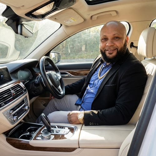 AI Design for Szerkeszd meg ezt a képet úgy benne ül 1 BMW luxus osztályban. Arany nyaklánc és karóra legyen rajta és a kép 100%-ban valódi legyen az arc minden hasonlitson