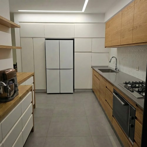 AI Design for Edit the kitchen image so the green cabinets are changed to natural wood, matching the same wood tone and finish as the surface above the cabinets on the opposite side of the kitchen. Replace the wall tiles with white ceramic tiles featuring a more refined, subtle, and elegant pattern. Keep the overall design cohesive, realistic, and consistent with the original lighting and proportions.”