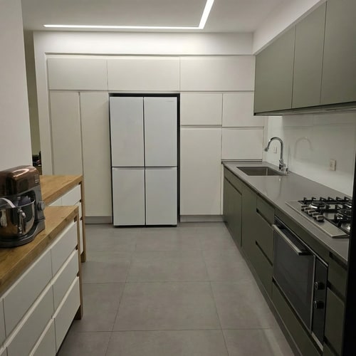 AI Design for Edit the kitchen image so the cabinets in the sink area are changed to a dark khaki green color. Change the countertop to a healthy gray tone. Modify the upper cabinets above the work surface so they are taller and match the same height as the cabinets in the refrigerator area, creating a uniform and continuous cabinet height throughout the entire kitchen. Keep the overall layout, lighting, and materials realistic and consistent with the original image.”