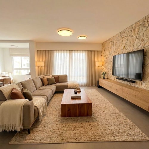 AI Design for A cozy and elegant living room featuring a full-length sofa adorned with textured blankets and soft throw pillows, paired with a warm wood coffee table — Wide-angle interior shot with an expanded field of view to show the entire sofa and the full expanse of the large window area, A harmonious palette of warm earth tones, rich wood grains, and creamy neutrals, Soft ambient lighting creating a warm, inviting, and comfortable atmosphere, Photorealistic interior design visualization with a focus on natural textures and elegant materials, Ensure the entire sofa and coffee table are fully visible within the frame without cropping; avoid cold or harsh lighting, A bright residential interior featuring a large window that provides a soft backdrop, grounded by a textured, warm-toned area rug.