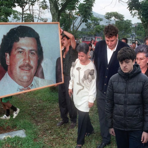 AI Design for Pon a la persona de la imagen 2, la que esta sonriendo, en la imagen 1. NO cambies nada de la imagen 1, solo pon a la persona incorporada en el grupo de personas de la imagen 1. y que este triste. Pero la persona tiene que tener la misma cara y el mismo formato de color de la foto