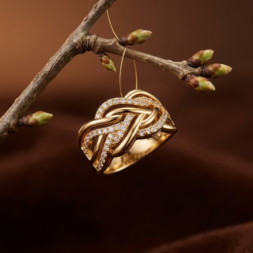 AI Design for ultra realistic luxury jewelry photography of a single elegant gold diamond ring suspended from a natural tree branch with small fresh buds warm deep brown gradient background