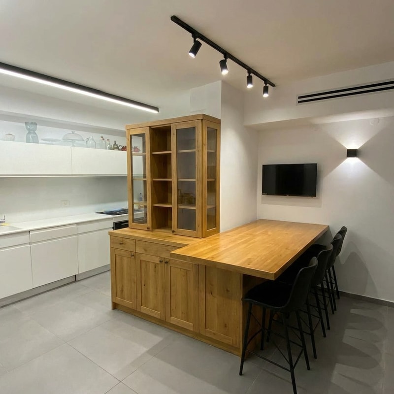 This is a dining area that we would like to redesign.
The butcher block worktop will be moved approximately 30 cm to the left, toward the kitchen. The shape of the countertop will be modified: instead of having a waterfall edge, it will feature a lowered surface at a height of 75 cm. The countertop will also function as part of the cabinet design.
In the attached drawings, each image shows a different elevation view.
The cabinet will be designed in a rustic style.
The lower section will have solid, closed cabinets.
The upper section will feature hinged glass doors.
Cabinet depth: approximately 40 cm
Cabinet width: 80 cm
Wall width: 100 cm
The cabinet finish will be in a light brown tone that complements the natural wood tone of the butcher block.
Seating should be arranged around the butcher block, as it will function as a dining table.
Currently, the butcher block height is 90 cm. We would like to lower it to 73 cm, which is standard dining table height.
The existing lighting fixture above the butcher block should be removed. Instead, install a black track lighting system with adjustable spotlights.