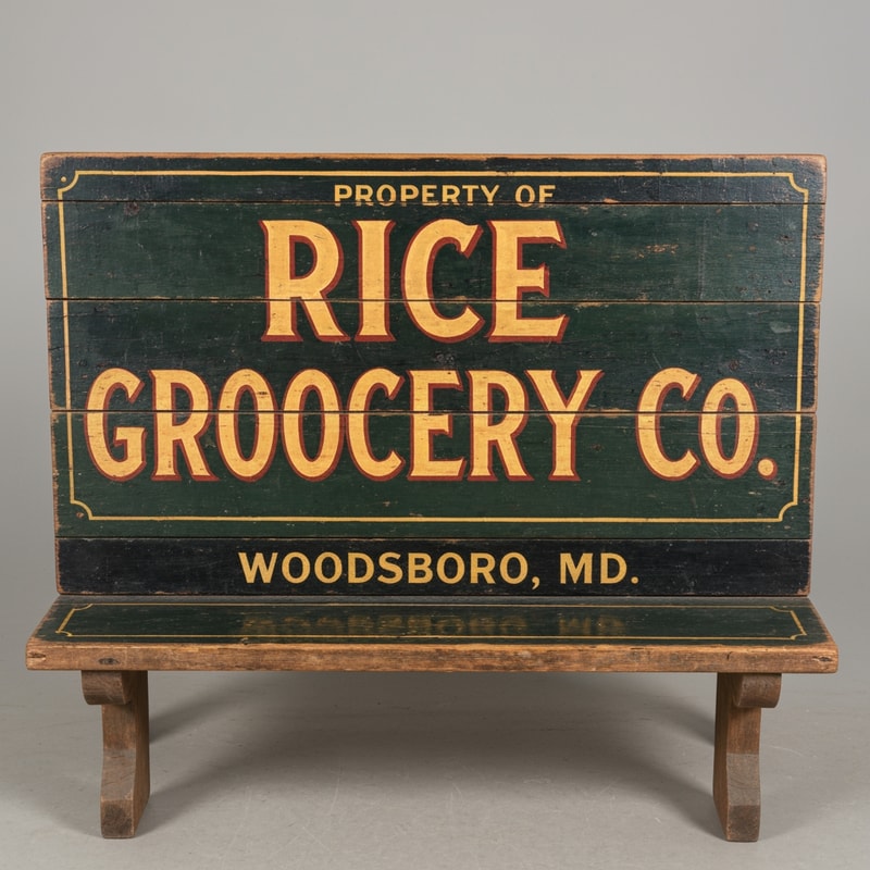A vintage wooden bench designed like an old general store advertising sign, viewed straight from the front (perfect frontal view, no perspective distortion). The top surface is flat and clearly visible like a signboard. It has hand-painted, slightly worn lettering in a classic 19th-century style. The main text reads “Rice Grocery Co.” in large, bold, warm yellow and red lettering. Above it in smaller text: “Property of”. Below it: “Woodsboro, MD.” The wood is aged, slightly weathered with visible grain and subtle paint wear. Colors are dark green, black, and rustic tones. The bench has simple wooden legs visible underneath. Lighting is soft and natural, background neutral and unobtrusive.